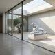 A modern minimalist interior showcases the Giant Sculptures Calm Lying Dog Marble Outdoor Sculpture (90cm) on a pedestal by floor-to-ceiling windows, overlooking a courtyard with an olive tree and gravel for added elegance.