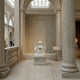 The Reading Grace Angel Marble Outdoor Sculpture - 120cm by Giant Sculptures sits elegantly in a grand museum hall, illuminated by skylight, with a plaque beside this exquisite marble angel figure reading a book.