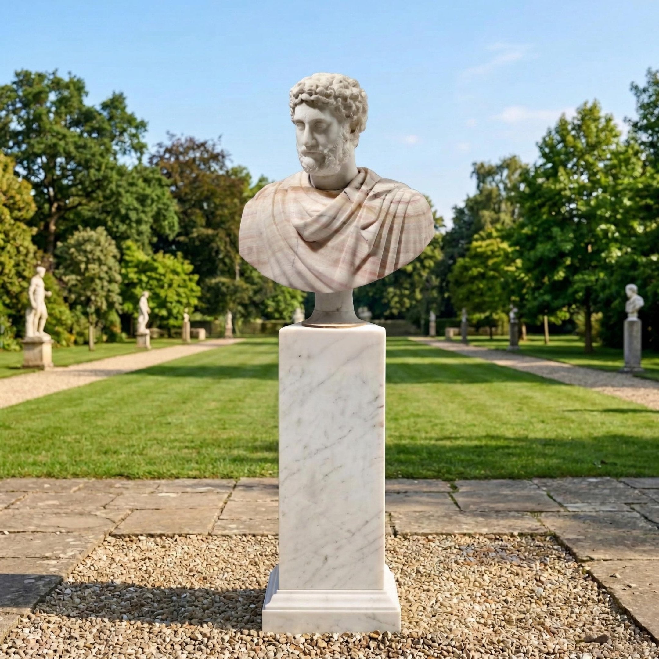The Marcus Aurelius Marble Bust Sculpture (65cm) by Giant Sculptures stands on a pedestal in a formal garden with manicured lawns, gravel paths, and trees under a clear sky.