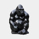 The Onyx Seated Gorilla Marble Outdoor Sculpture - 80cm by Giant Sculptures features a glossy gorilla sitting with arms on its knees and a focused expression, crafted from Black Dali Marble and standing out against any simple background.