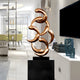 Copper abstract sculpture art featured in a contemporary home, standing on a black pedestal, reflecting its flowing design and modern aesthetic, ideal for sophisticated decor.