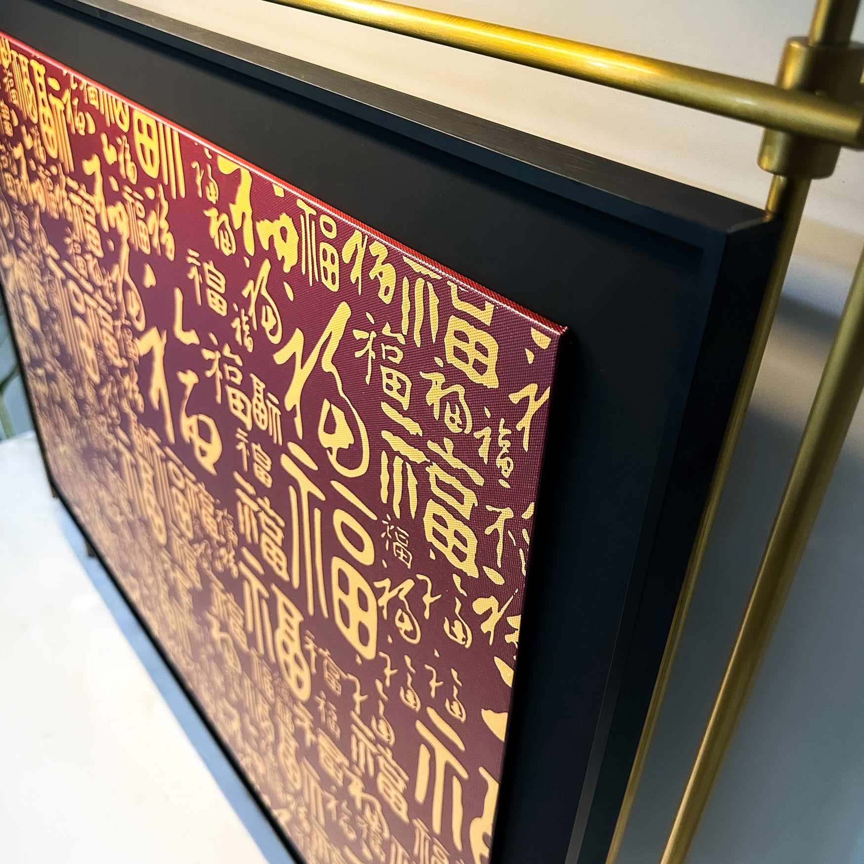 The Celestique Prosperity Script Framed LED Wall Art by Giant Sculptures features a close-up of gold Chinese calligraphy on a red background, symbolizing prosperity. Supported by a gold stand, the dense characters form a patterned artwork when viewed from above.