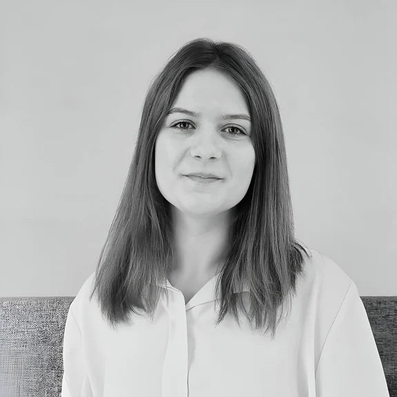 A woman with shoulder-length hair smiles slightly in a black and white portrait. She is wearing a light-colored shirt and is seated against a plain backdrop, creating a simple and professional appearance.