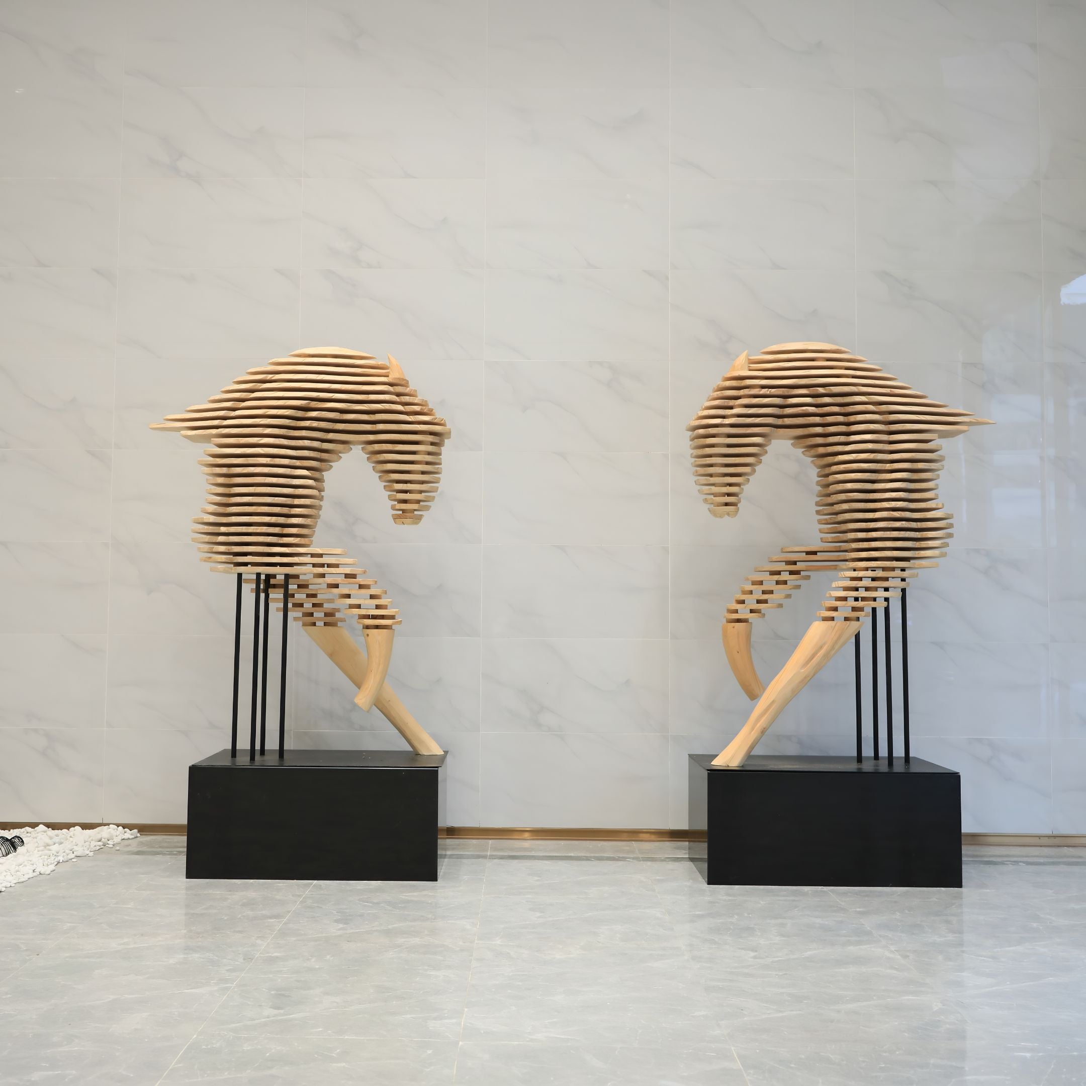 Rising Stallion Wood Horse Sculpture by Giant Sculptures, a pair of 160cm layered wood horse head forms on black bases in a marble-walled lobby.