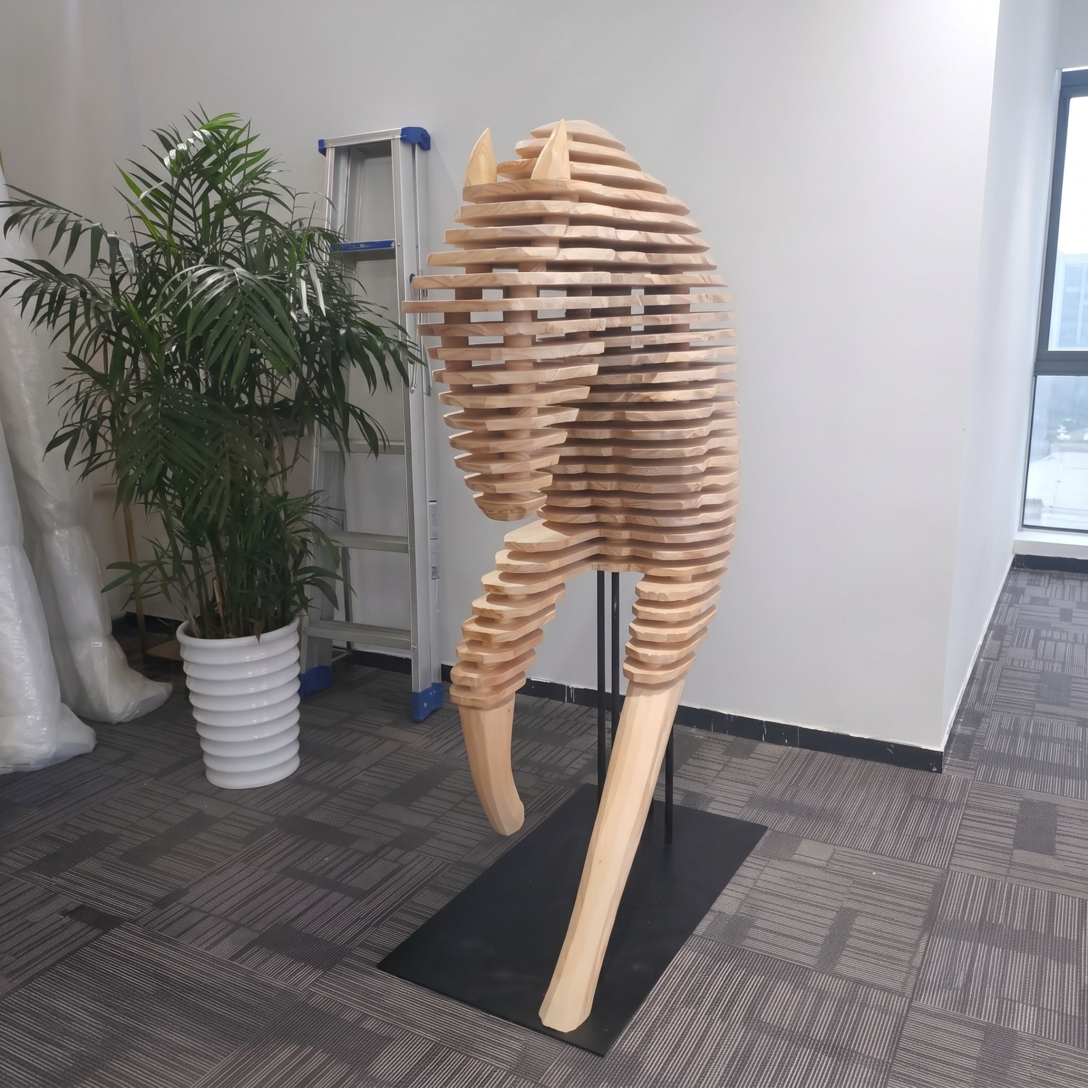 Rising Stallion Wood Horse Sculpture 160cm by Giant Sculptures, rear view of layered wood slab horse on black base, beside a potted palm and ladder in an office.