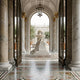 Weeping Angel Marble Outdoor Sculpture by Giant Sculptures, draped over a tomb in a marble colonnade with a tiered fountain and olive trees beyond.