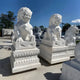 Under a clear blue sky, Giant Sculptures Chinese Guardian Lion III Marble Outdoor Sculptures (200cm) are majestically placed on large pedestals. The statues feature detailed manes and fierce expressions, with trees in the background enhancing the scene.