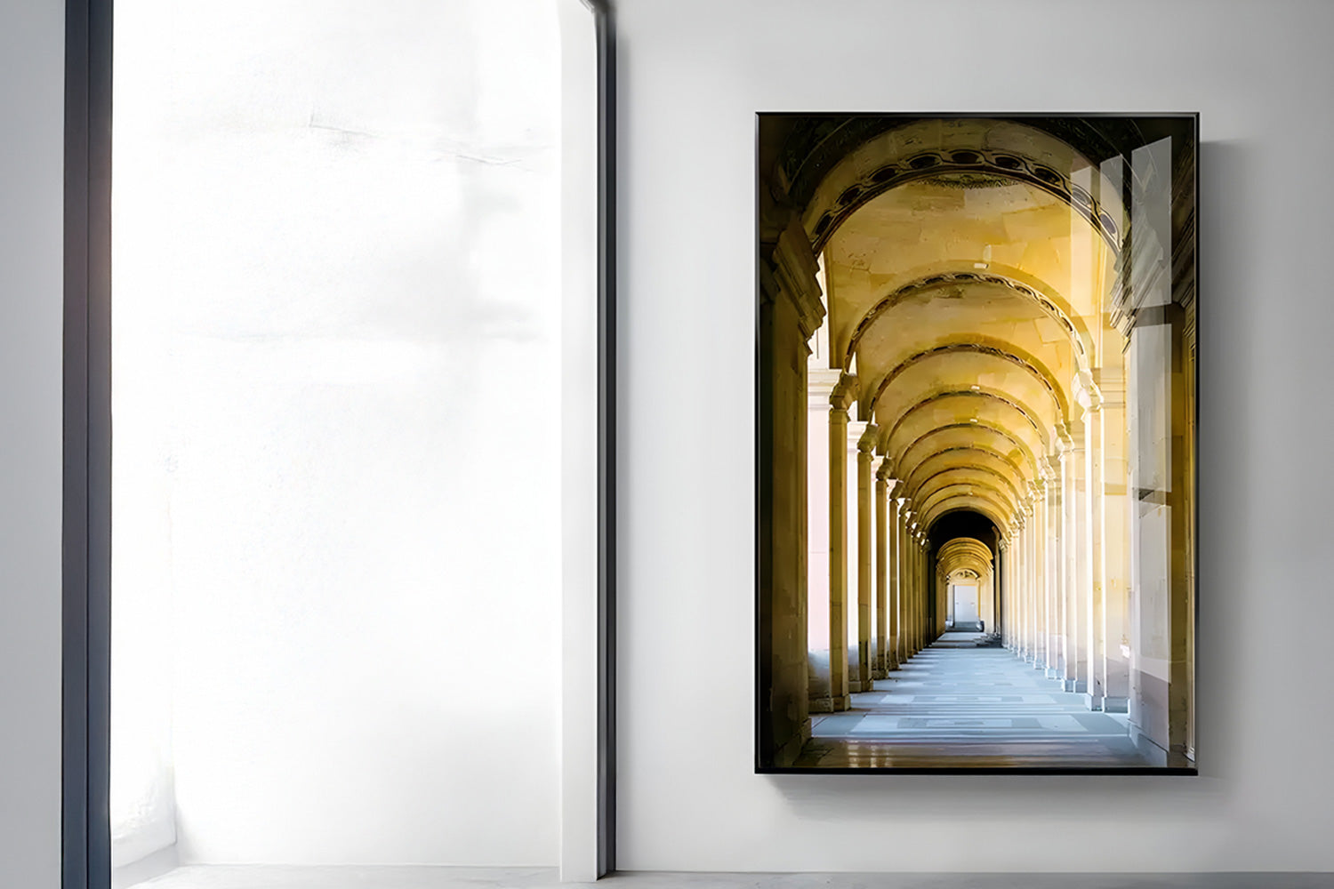 A photograph hanging on a white wall depicting a long, arched corridor with golden lighting. The image reflects classical architecture with columns lining both sides, leading to a distant vanishing point. Natural light illuminates the room.