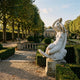 Giant Sculptures Woman on Crescent Moon 80cm white marble statue on a stone plinth in a formal garden with topiary, balustrade, and orangery beyond.