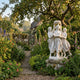 Giant Sculptures' Three Dancing Women with Floral Wreath Marble Sculpture on a weathered stone plinth in a cottage garden with apple tree and foxgloves.