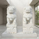 Two Chinese Guardian Lion IV Marble Outdoor Sculptures by Giant Sculptures, each 180cm tall and hand-carved from white marble, are displayed side by side on pedestals in a modern indoor space with light walls and garden views.
