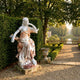 Seated Classical Woman Marble Sculpture 130cm by Giant Sculptures in white and warm brown marble, displayed on a stone plinth in a formal garden beside a hedge.