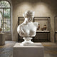 The Classical Female Marble Bust Sculpture - 75cm by Giant Sculptures is displayed on a pedestal in a museum room, surrounded by ancient pottery and illuminated by light from a large arched window in the background.