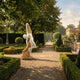 Dancing Goddess Marble Sculpture 160cm by Giant Sculptures in white and amber marble, posed with arched back and flowing drapery, on a gravel garden pathway.