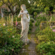 Goddess of Harvest Marble Sculpture by Giant Sculptures, 160cm female figure in flowing drapery with floral crown, on a stone path in a cottage flower garden.