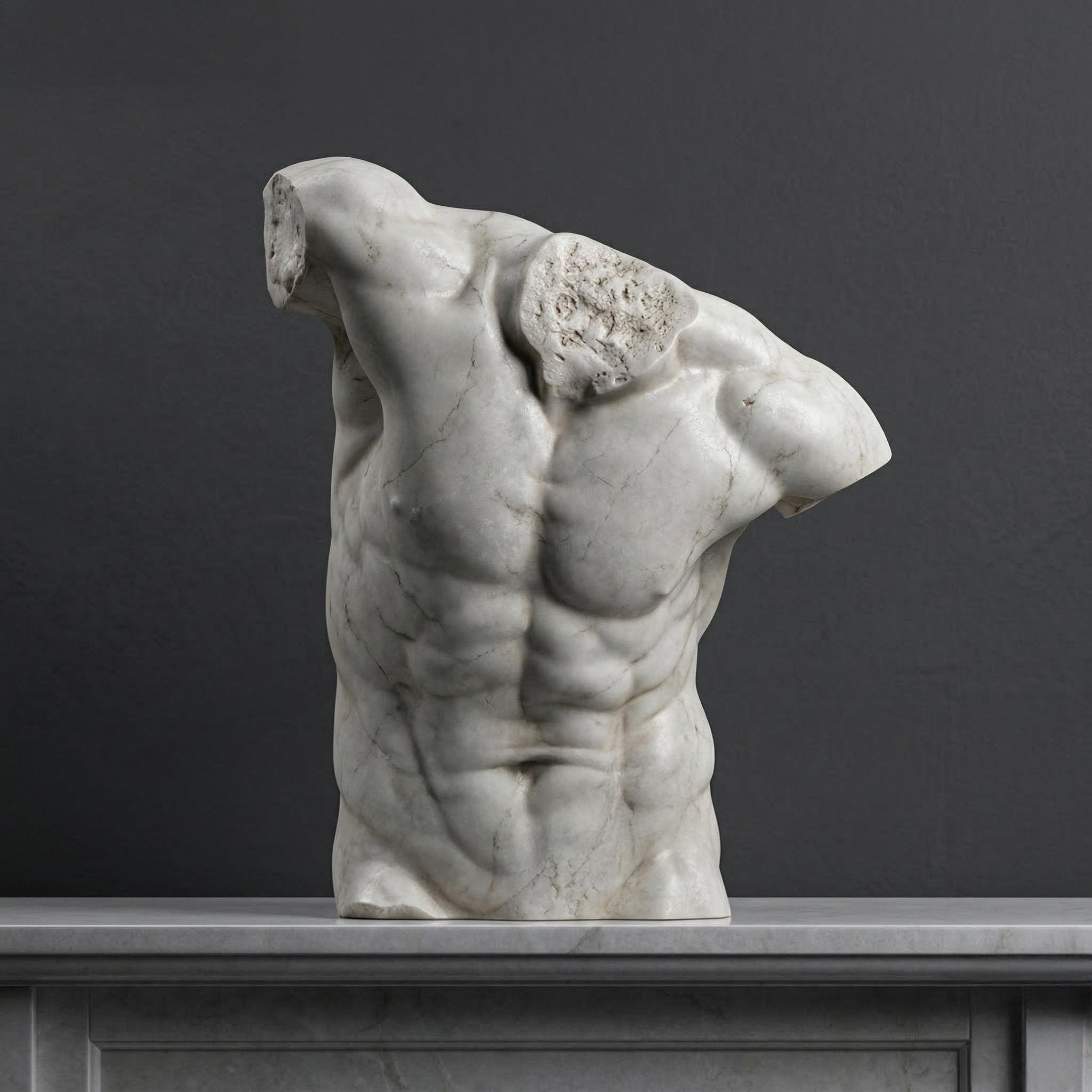 The Male Marble Torso Sculpture - 80cm by Giant Sculptures, featuring detailed musculature and a classical style, is displayed headless and armless on a gray stone surface against a dark gray background.