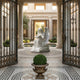 The Heavenly Reading Angel Marble Outdoor Sculpture - 120cm by Giant Sculptures features a graceful marble angel reading at the center of a courtyard with ornate iron gates, mosaic floor, columns, and lush greenery for a tranquil garden scene.