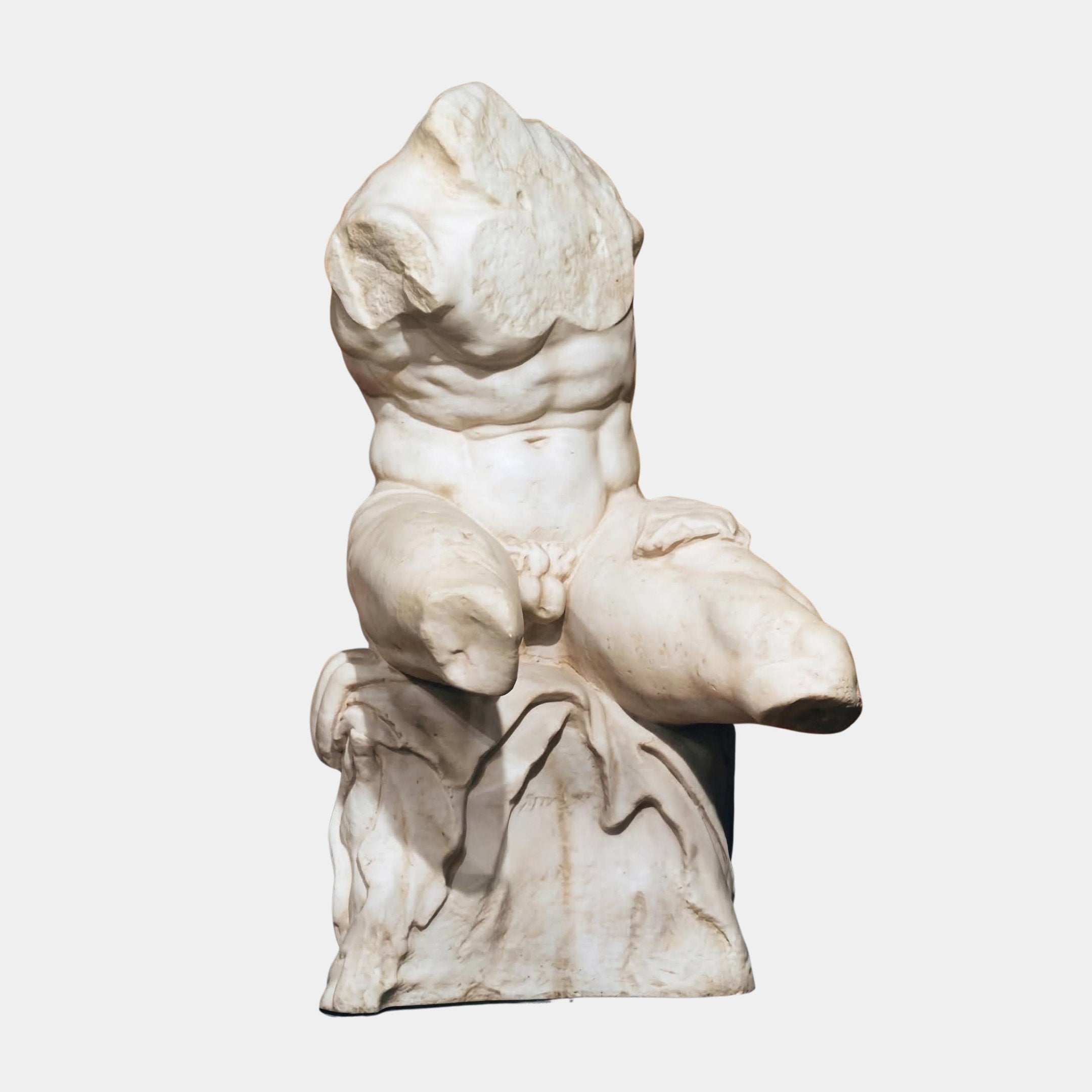 Seated Male Marble Torso Sculpture in natural white marble showing a muscular headless torso with draped waist, seated on a stone base, against a plain light background.