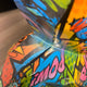 Colorful close-up of the Giant Sculptures Pop Art Gorilla Sculpture - 50cm (Ex Display) with comic-style art, bold shapes, vibrant blue, orange, and green areas, and "IMOO" in pink—an eye-catching piece for modern interiors.
