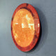 Galaxia Sun Crystal Porcelain LED Wall Art by Giant Sculptures shown at an angle on a grey wall, its round amber and golden marbled surface glowing with concealed rear LED backlighting and a thin red-toned frame.