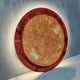 Galaxia Sun Crystal Porcelain LED Wall Art by Giant Sculptures leaning against a grey wall, showing a round amber and golden sun design with dark red corona edge and warm LED backglow.