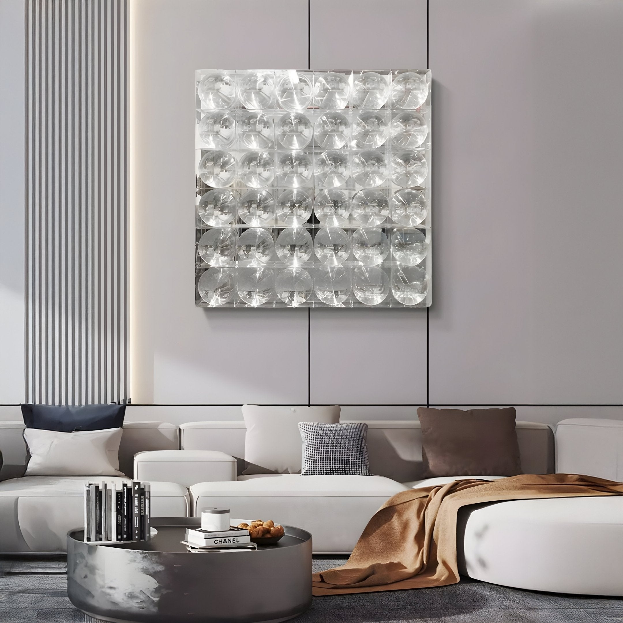 A modern living room featuring a light gray sectional sofa, assorted pillows, a brown throw, a round coffee table with books, and Giant Sculptures’ Haloid IV Bubble Grid Acrylic 3D Wall Art with bold metallic circular patterns.