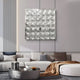 A modern living room featuring a light gray sectional sofa, assorted pillows, a brown throw, a round coffee table with books, and Giant Sculptures’ Haloid IV Bubble Grid Acrylic 3D Wall Art with bold metallic circular patterns.