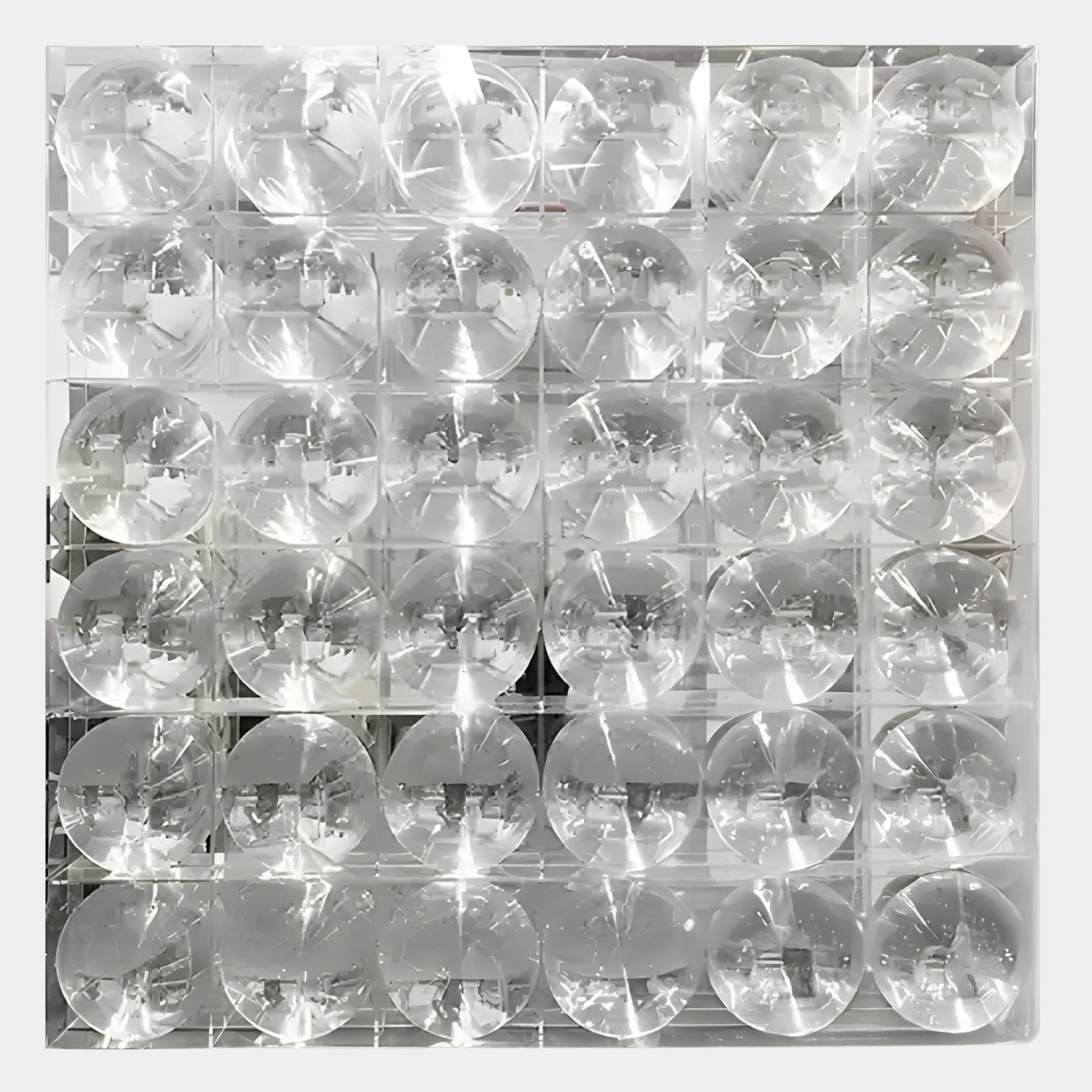 The Haloid IV Bubble Grid Acrylic 3D Wall Art by Giant Sculptures features 36 clear, round acrylic lenses arranged in a 6x6 grid, creating captivating optical wall decor that reflects and distorts light into abstract patterns.