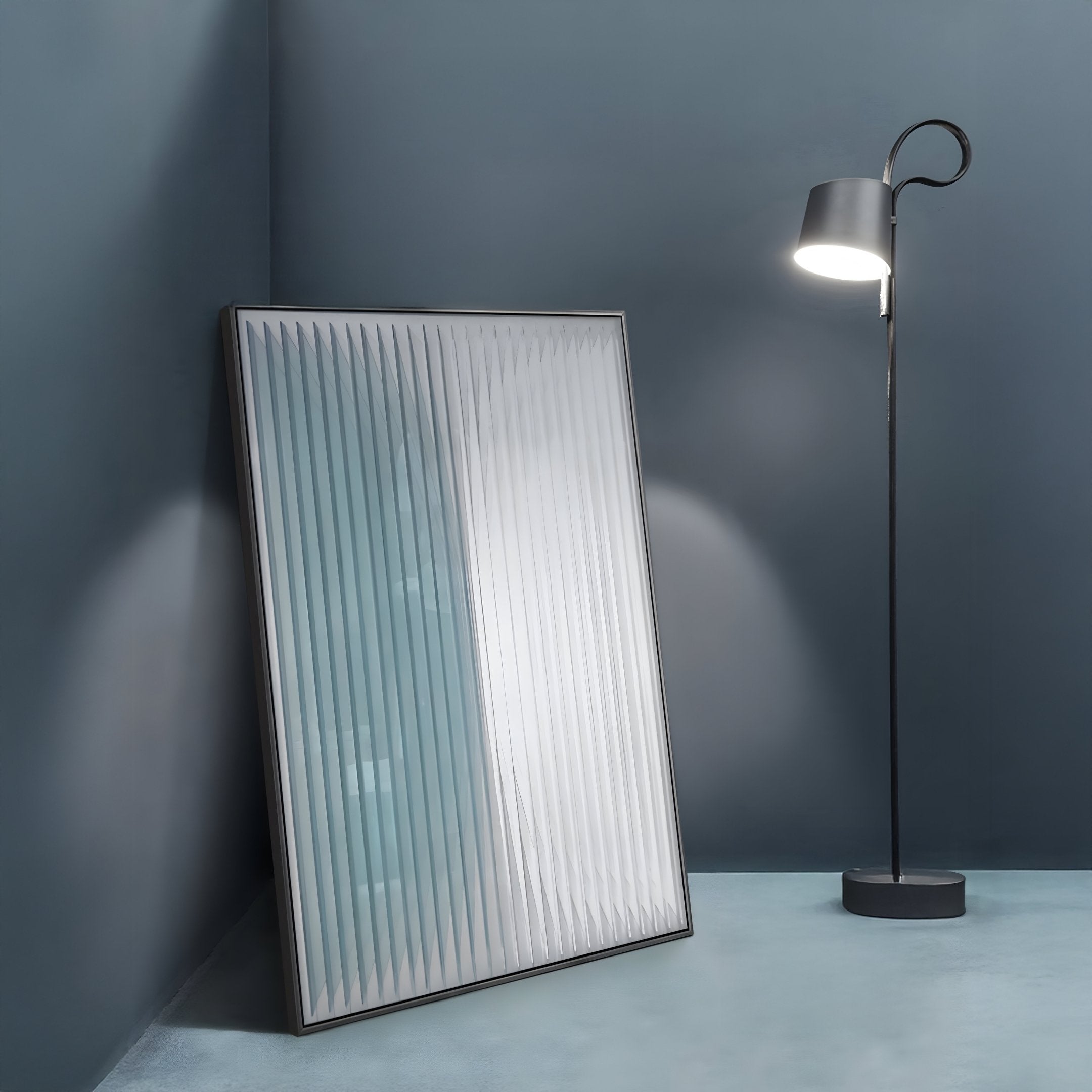 A tall black floor lamp with a curved neck stands lit next to the Verta Blue Gradient Acrylic 3D Wall Art by Giant Sculptures, which features textured vertical lines and leans against a blue-gray wall in the corner.