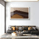 A modern living room features a black leather sofa, neutral pillows, a round coffee table, and dried flowers. Above the couch is Giant Sculptures Tessera Caramel & Walnut Gradient Acrylic 3D Wall Art, adding depth with its brown and beige tones.