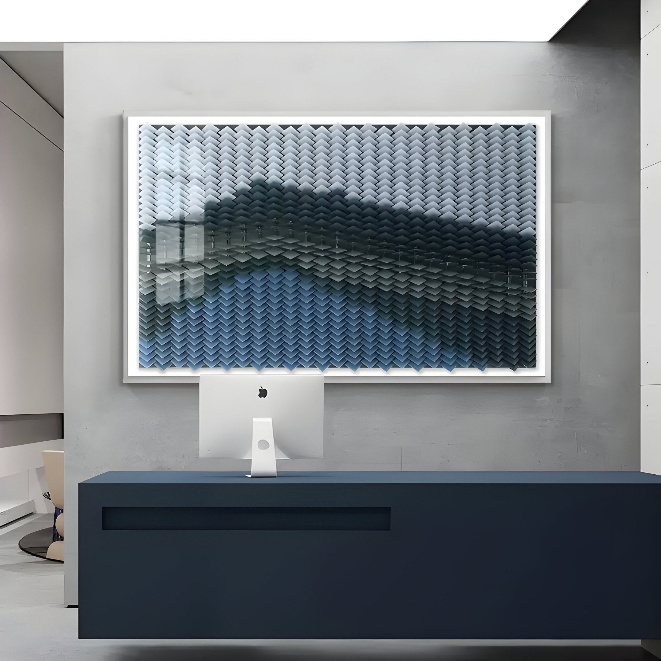 A modern office reception area features a sleek dark blue desk, a white iMac, and the Giant Sculptures Tessera Frosted & Midnight Blue Gradient Acrylic 3D Wall Art with a wave-like texture on a gray concrete wall.