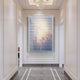A modern hallway with white walls and gold trim features the Chromat Sunset Mauve Glow Acrylic 3D Wall Art by Giant Sculptures—horizontal white slats over pastel hues. The floor displays a geometric white border on gray marble tiles.
