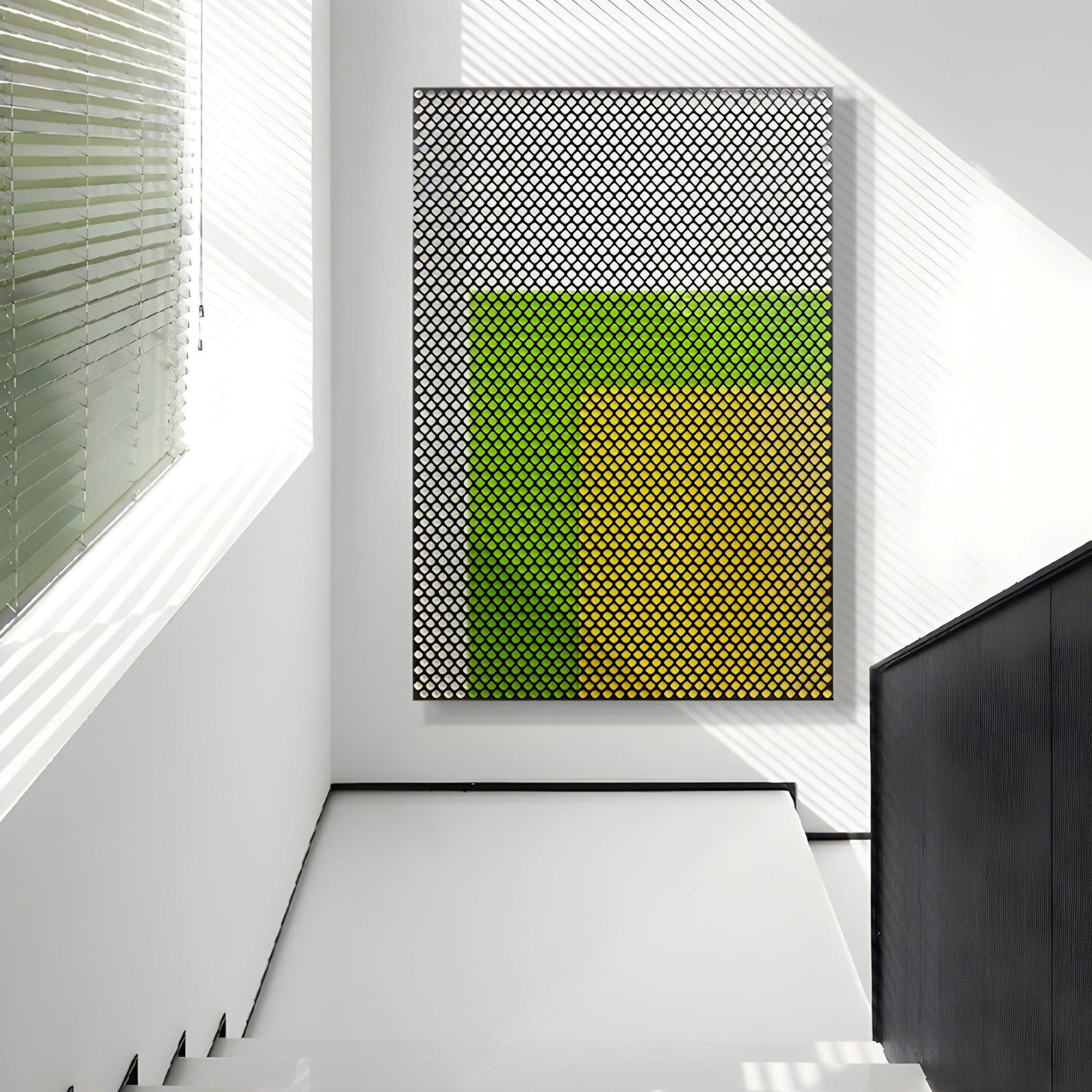 A minimalist, sunlit hallway with white walls, a staircase on the right, and Giant Sculptures’ Pixelate Lime Gold Acrylic 3D Wall Art—featuring a green-yellow gradient with a black grid—hanging on the wall.
