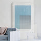 A modern living room with a light blue sofa and cozy throw features the Pixelate Sky Frost Acrylic 3D Wall Art by Giant Sculptures—a grid of white circles on a blue gradient—mounted above a small glass table on a white wall.
