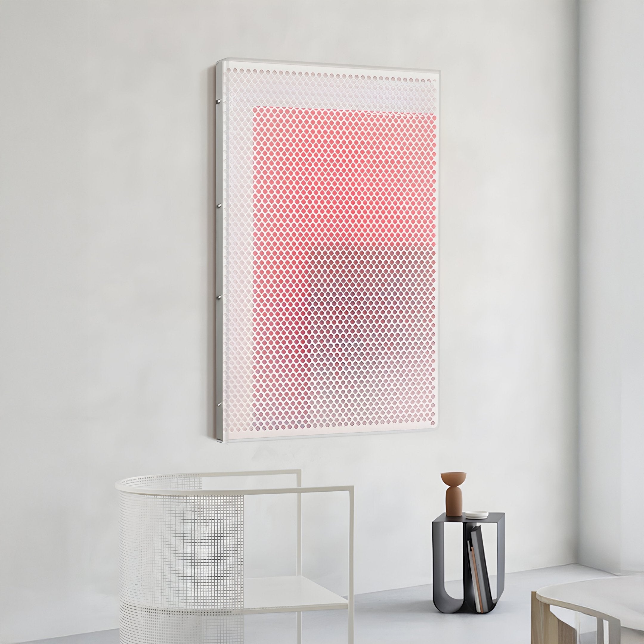 A modern, minimal room featuring the Pixelate Scarlet Blush Acrylic 3D Wall Art by Giant Sculptures—a bold grid of red circles fading to white—paired with a white mesh chair, small gray table, and brown vase for a balanced touch.