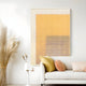 A modern living room with a white sofa, beige and peach pillows, a small side table with a vase, tall pampas grass, and Giant Sculptures’ Pixelate Amber Rust Acrylic 3D Wall Art showcasing bold yellow and white honeycomb patterns.