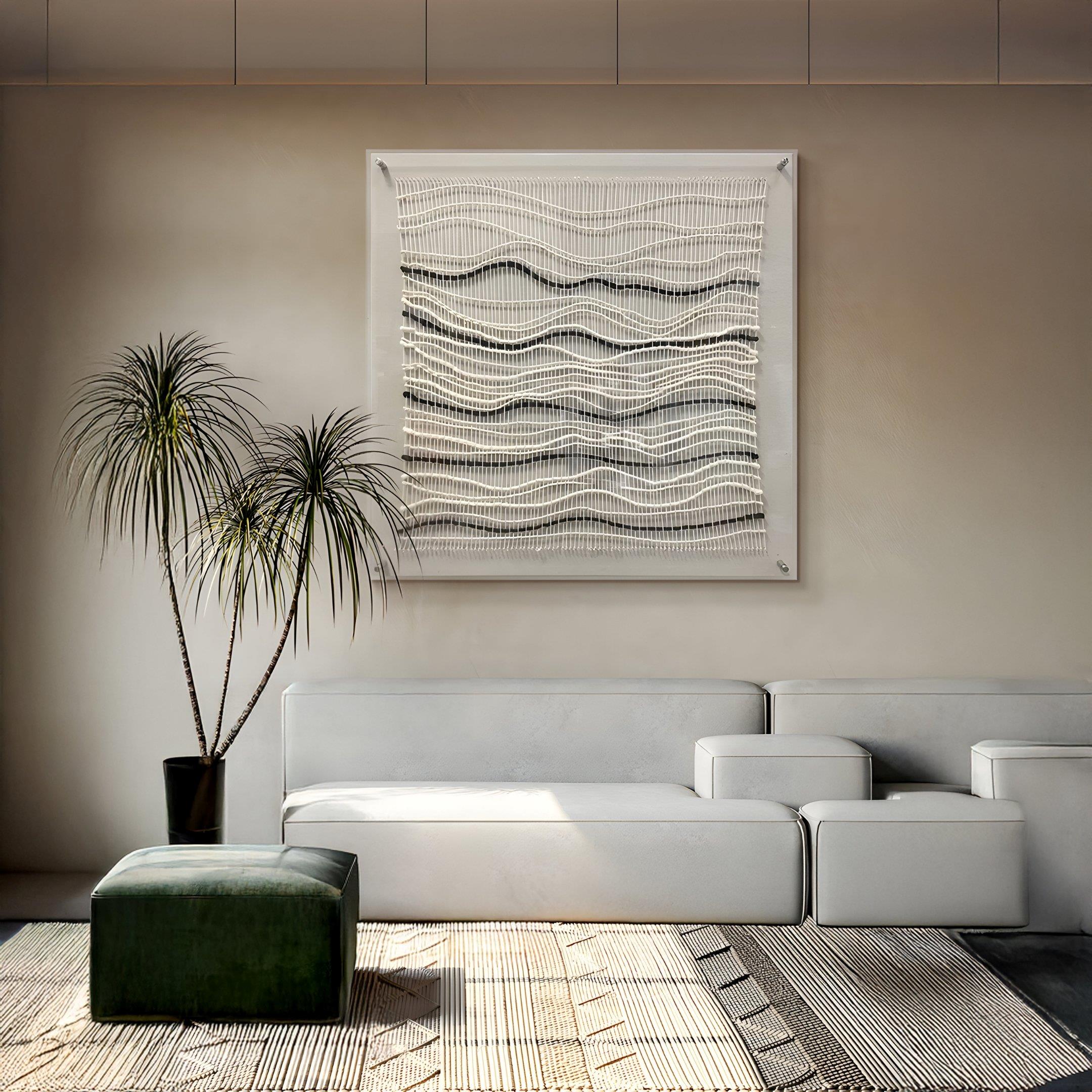 A modern living room with a white sectional, green ottoman, tall potted plant, and Tanglewave Ivory & Charcoal Ripple Texture Acrylic 3D Wall Art by Giant Sculptures. Neutral tones and sunlight create a calm, minimalist feel.