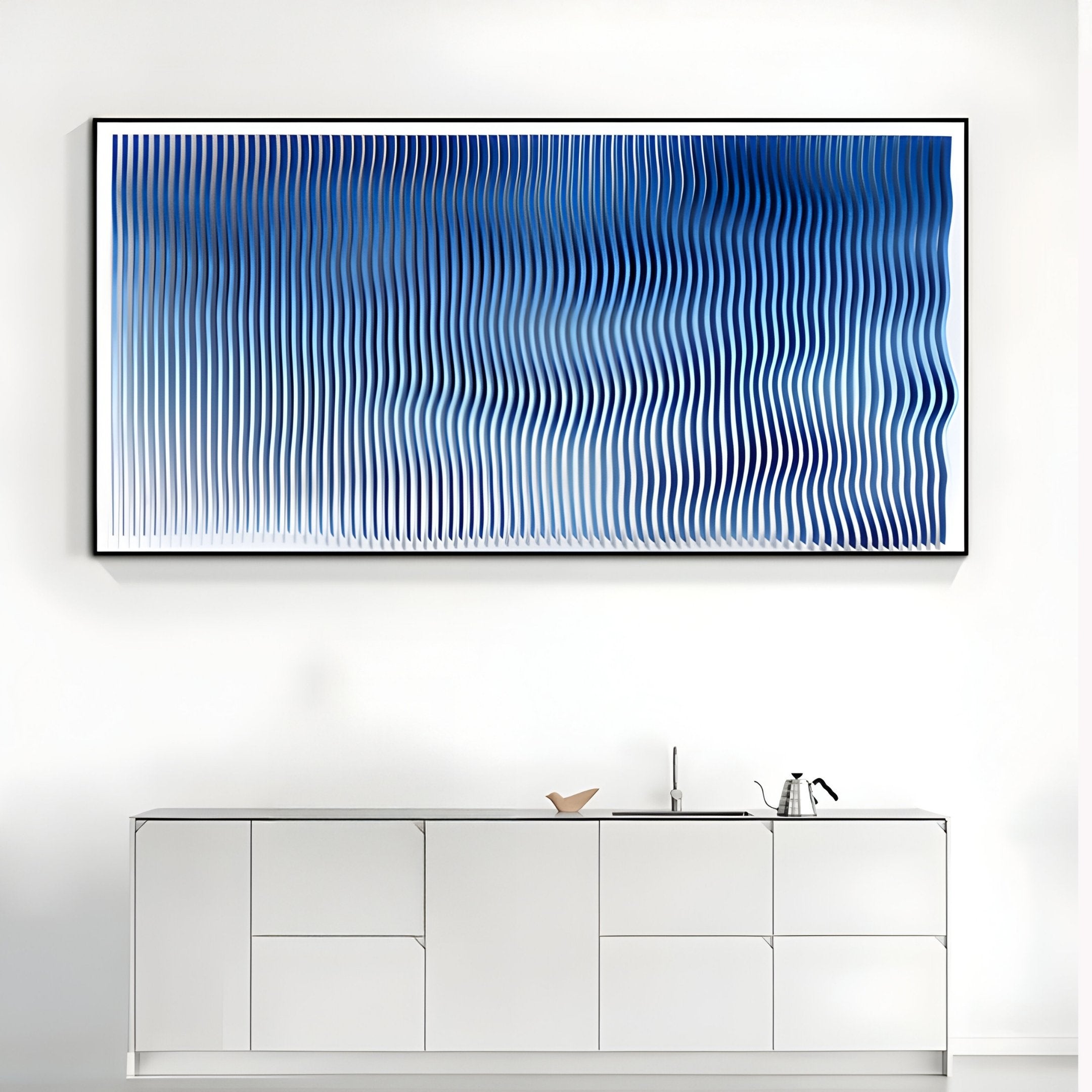 A modern kitchen features a white minimalist cabinet with a kettle and decor. Above, the Giant Sculptures Current II Navy Sky & Icy White Acrylic 3D Wall Art adds an artistic touch with wavy blue lines on a light background.