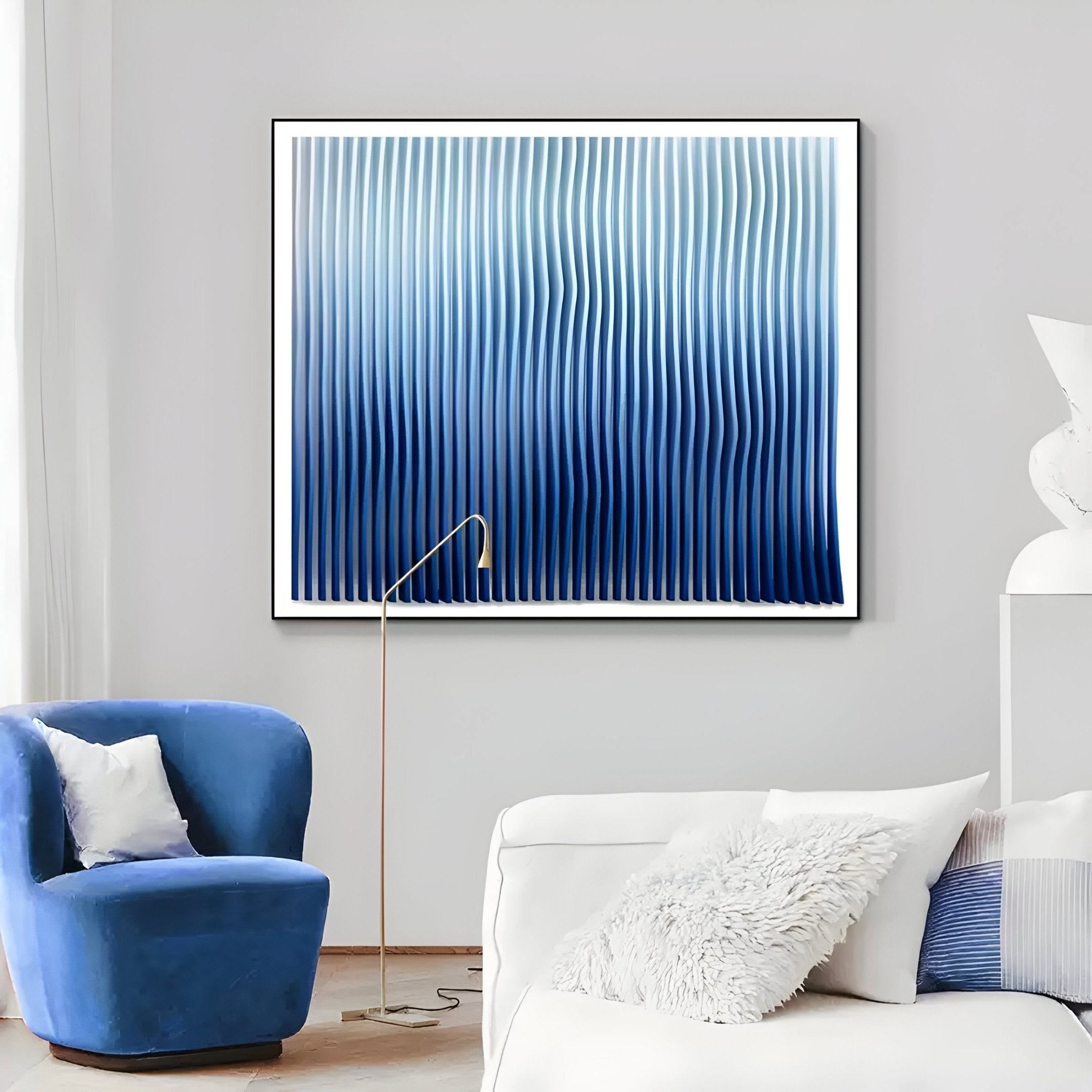 A modern living room with a white couch, blue velvet chair, gold floor lamp, and Giant Sculptures’ Current III Navy Sky & Icy White Acrylic 3D Wall Art featuring vertical blue and white wavy lines on the light gray wall.