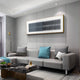 A modern living room with a sleek gray sectional, colorful pillows, a marble coffee table, bright lighting, minimalist decor, a gold floor lamp, and Giant Sculptures Flowline Slate Blue Gradient Acrylic 3D Wall Art.
