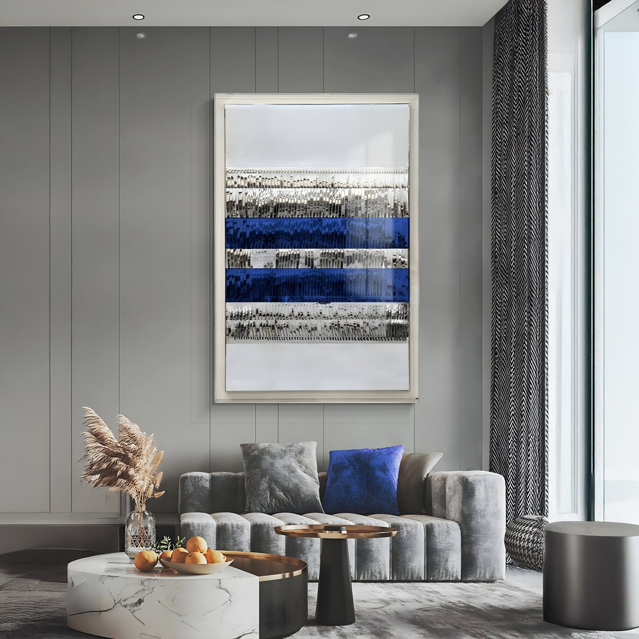 A modern living room with a gray sofa, blue and gray pillows, marble coffee table with fruit, and Giant Sculptures Rhythm Sapphire & Silver Layered Stripe Leather 3D Wall Art on a gray paneled wall. Tall windows highlight the elegant artwork.