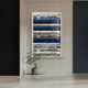 A potted plant rests on a light floor near a window with an abstract privacy covering of black, white, blue, and yellow stripes. The Rhythm Sapphire & Gold Layered Stripe Leather 3D Wall Art by Giant Sculptures adorns the white and dark navy walls.