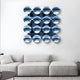 A modern living room with a white sectional sofa and the Giant Sculptures Dome Ice Blue Acrylic 3D Wall Art—16 reflective blue discs in a 4x4 grid—mounted above. A small round table sits to the right.