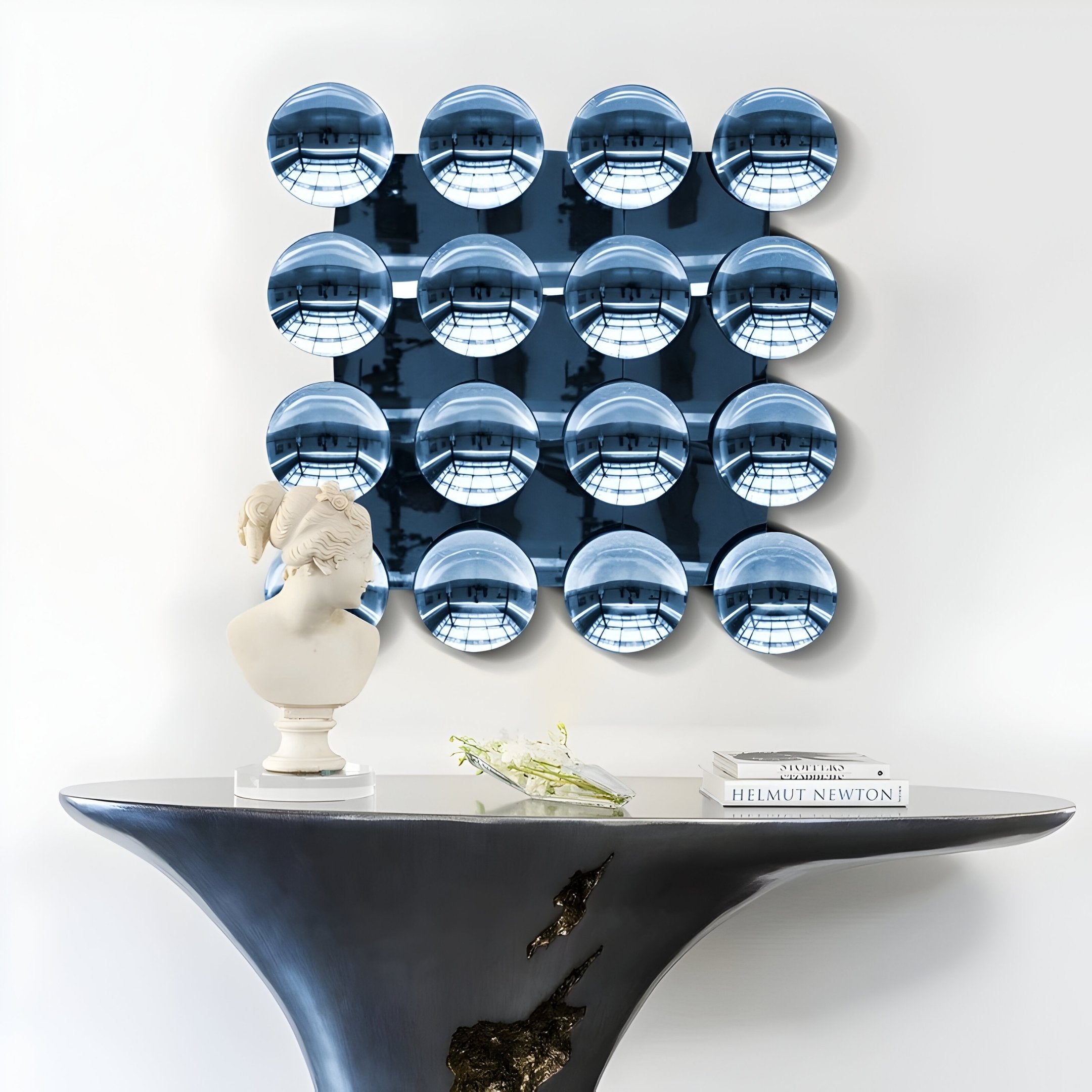 A modern entryway showcases a sculptural black console, a classical white bust, an art book, and Dome Ice Blue Acrylic 3D Wall Art by Giant Sculptures—a striking 4x4 grid of blue convex mirrors that adds depth and intrigue to the space.