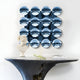 A modern entryway showcases a sculptural black console, a classical white bust, an art book, and Dome Ice Blue Acrylic 3D Wall Art by Giant Sculptures—a striking 4x4 grid of blue convex mirrors that adds depth and intrigue to the space.