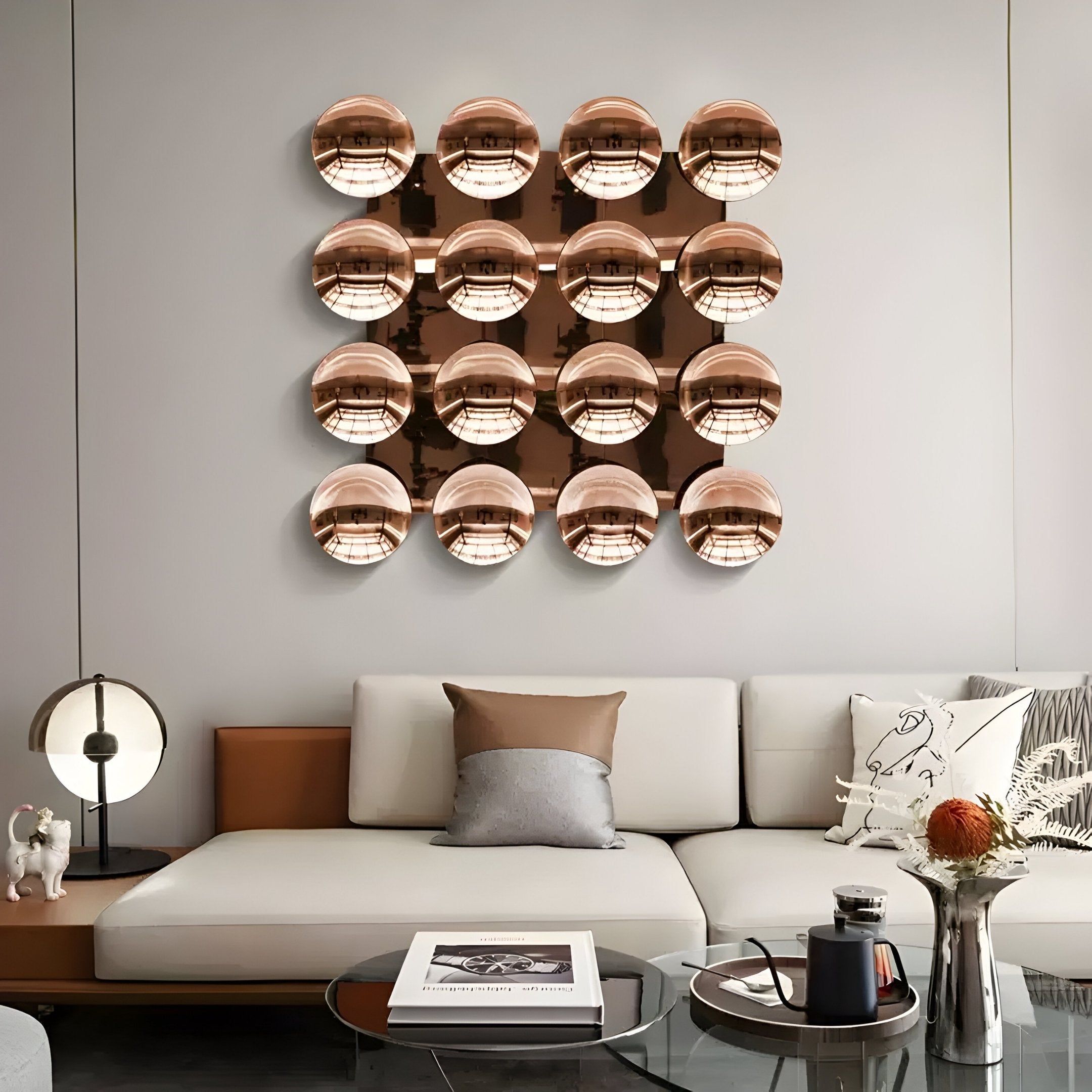 A modern living room with a white sectional sofa, decorative pillows, a small round table lamp, and Giant Sculptures Dome Burnished Copper Acrylic 3D Wall Art—a sculptural 4x4 grid of shiny round pieces—displayed above the couch.