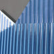 The Vertex Deep Navy & White Ridge Acrylic & Wood Carving 3D Wall Art by Giant Sculptures features blue and white ribbed panels arranged at varied angles, creating a bold geometric abstract pattern on a muted gray background.