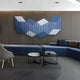 A modern lounge features a gray accent wall, Giant Sculptures Vertex Deep Navy & White Ridge Acrylic & Wood Carving 3D Wall Art, low blue seating, a gray armchair, two round nesting tables, and an open book for minimalist decor.
