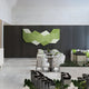 A modern dining area features white chairs, round tables, a dark accent wall, and striking geometric decor. The Vertex Green & Pale Mint Ridge 3D Wall Art by Giant Sculptures adds a fresh, contemporary touch with its green and white palette.