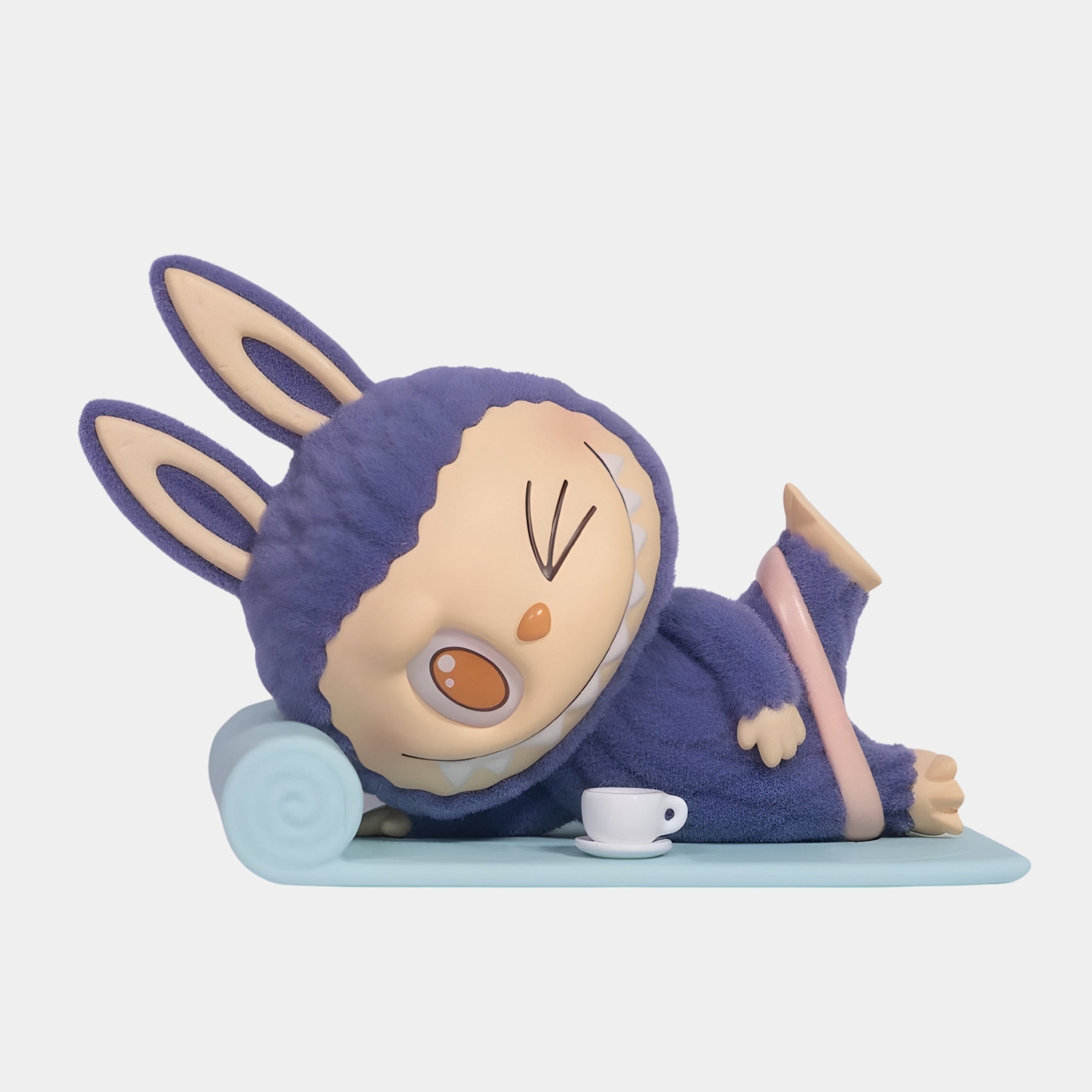 The Lazy Yoga Americano Labubu Sculpture - 160cm by Giant Sculptures features a character in a purple bunny costume, relaxed on a blue mat with a teacup, winking and smiling—ideal for an adorable indoor display.